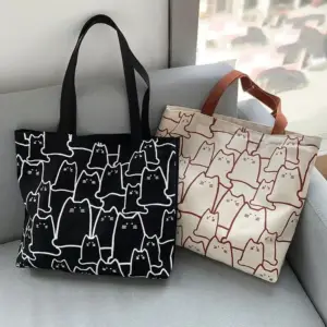 Zwei Canvas-Taschen mit Katzenmuster, schwarz und beige, auf grauem Sofa