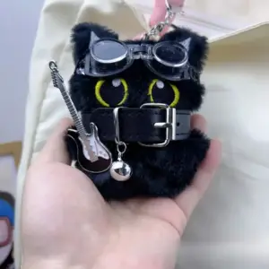 Schwarzer Katzenanhänger mit Brille, Halsband und kleiner Gitarre, in einer Hand gehalten