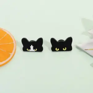 Zwei schwarze Katzen-Anstecker mit gelben Augen vor hellgrünem Hintergrund