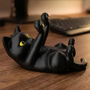 Schwarze Katzenfigur liegt mit erhobenen Pfoten als Handyhalter auf einem Holzschreibtisch