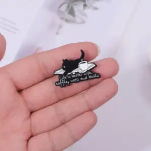 Schwarzer Emaille-Pin mit Katze, Buch und Kaffeetasse in der Hand